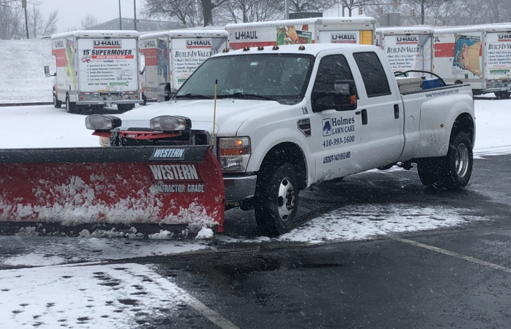 A white pickup truck equipped with a snow plow clearing snow.