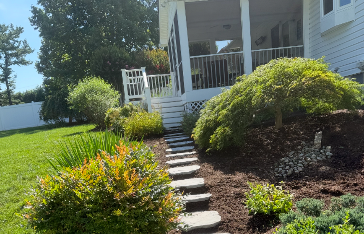 Stone pathway leading through a lush garden to a white porch.