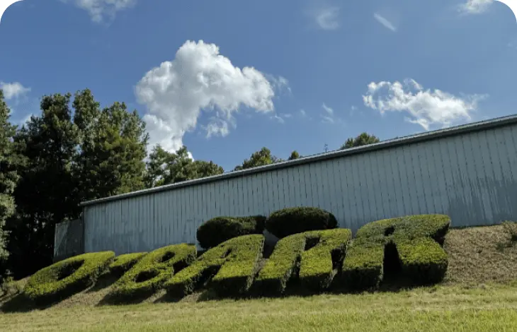 Bushes trimmed to spell 'LEADERS' under a blue sky with clouds.
