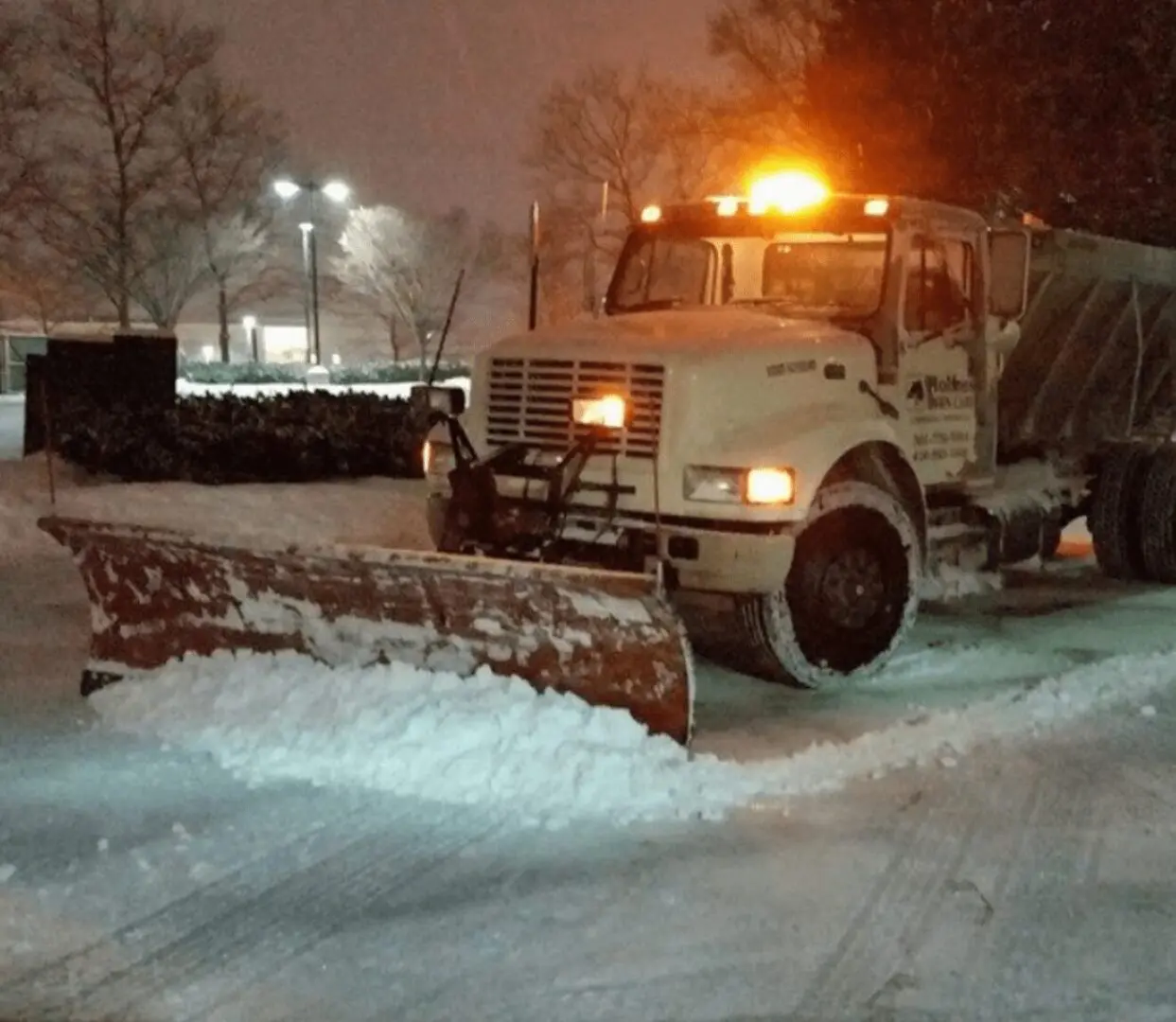 Snowplow clearing a snowy road at night with bright lights.