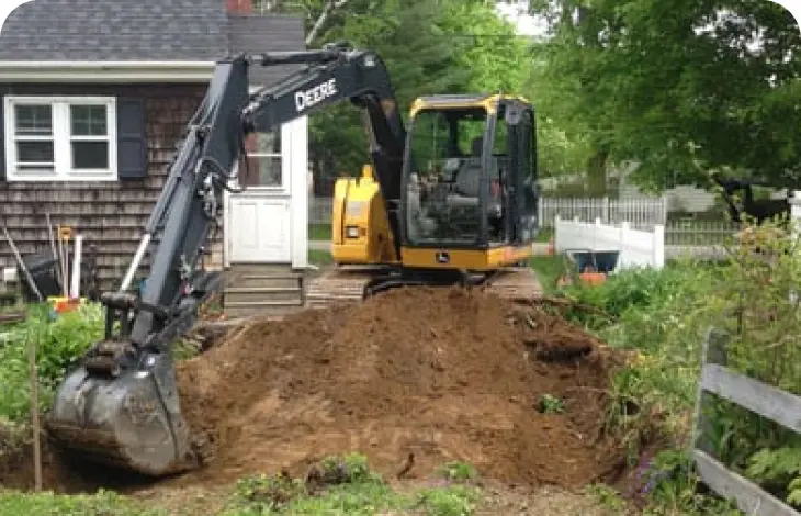 A yellow excavator digging soil near a house.