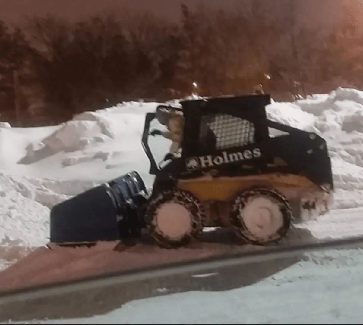 A skid steer loader clearing snow in a snowy area.
